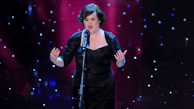 Susan Boyle canta frente a un micrófono con un vestido negro de lentejuelas