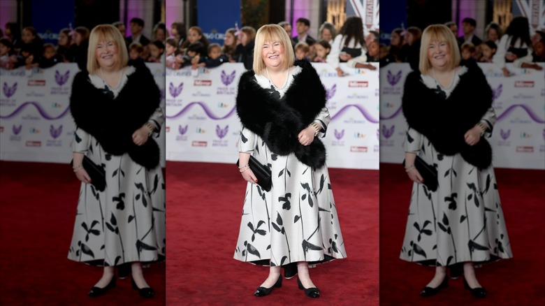 Susan Boyle sonríe con un bolero de piel negro y un vestido blanco y negro