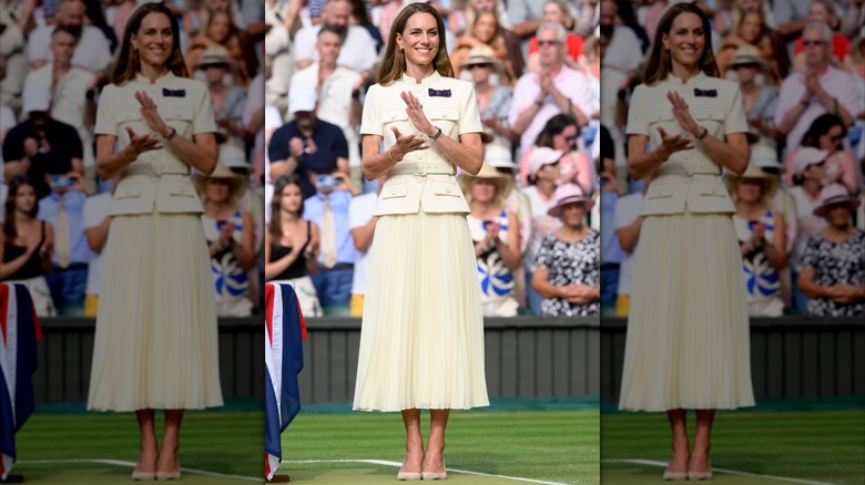 Kate Middleton aplaudiendo y vistiendo una falda plisada de color crema y un top con cinturón y botones en Wimbledon en 2025.