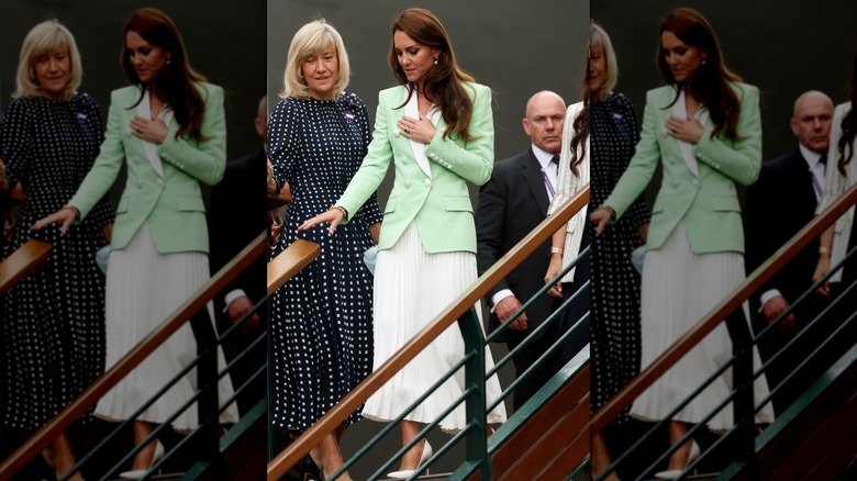 Kate Middleton bajando las escaleras con una falda plisada blanca y una chaqueta verde claro con ribetes blancos en Wimbledon en 2023.