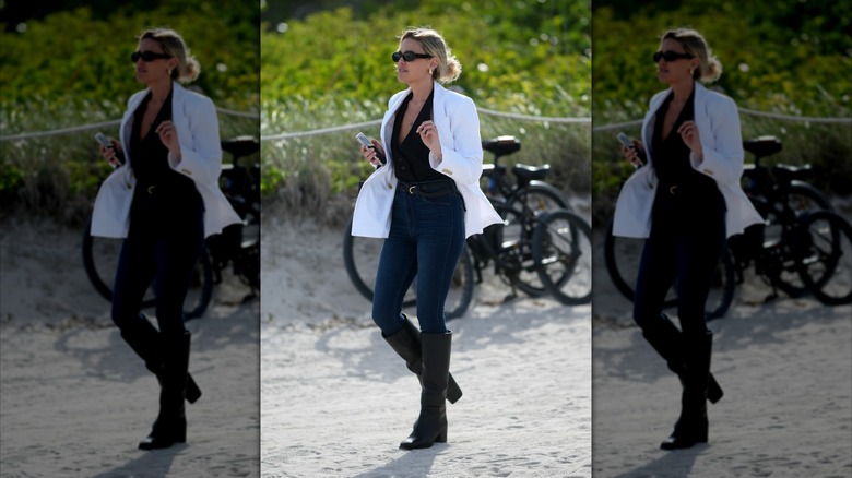 Una mujer vestida con jeans ajustados, botas negras y una chaqueta blanca.