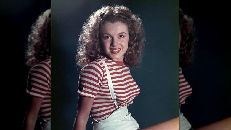 Marilyn Monroe posando en 1947 con una camisa a rayas rojas y blancas y pantalones cortos con tirantes blancos.