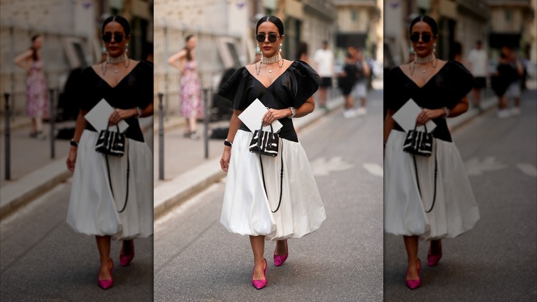 Una mujer que llevaba un vestido blanco y negro, una gargantilla de perlas de varios hilos, gafas de sol negras y tacones de color rosa brillante.