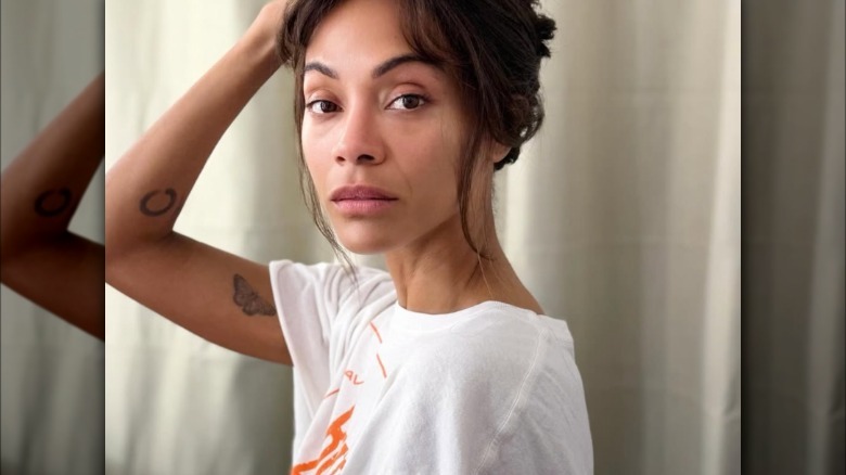 Zoe Saldana sin maquillaje con una camiseta blanca sujetando su cabello
