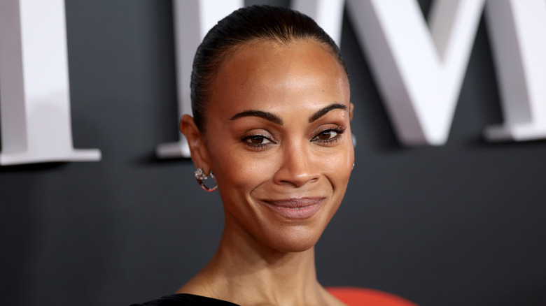 Zoe Saldana con un vestido negro con un moño peinado hacia atrás.