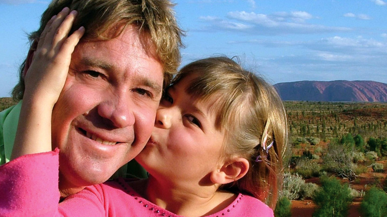 La joven Bindi Irwin con un top rosa besando a su padre, Steve Irwin, en la mejilla.