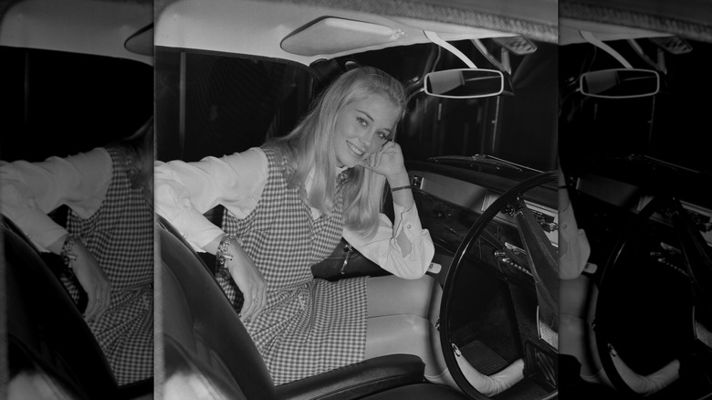 Una fotografía en blanco y negro de Cybill Shepherd sentada en un automóvil con un vestido a cuadros.