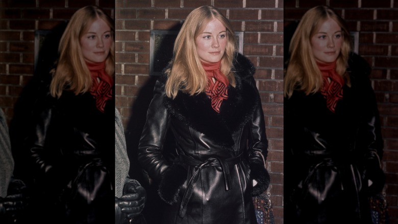 Cybill Shepherd con las manos en los bolsillos vestida con un abrigo de cuero Penny Lane y un pañuelo rojo.