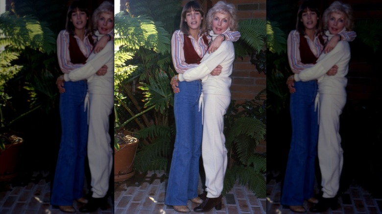Jamie Lee Curtis vistiendo jeans acampanados, una camisa a rayas y un chaleco marrón con Janet Leigh vistiendo un traje blanco en 1979.