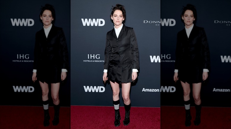Kristen Stewart luciendo un vestido de chaqueta negra con zapatos negros en un evento de alfombra roja.
