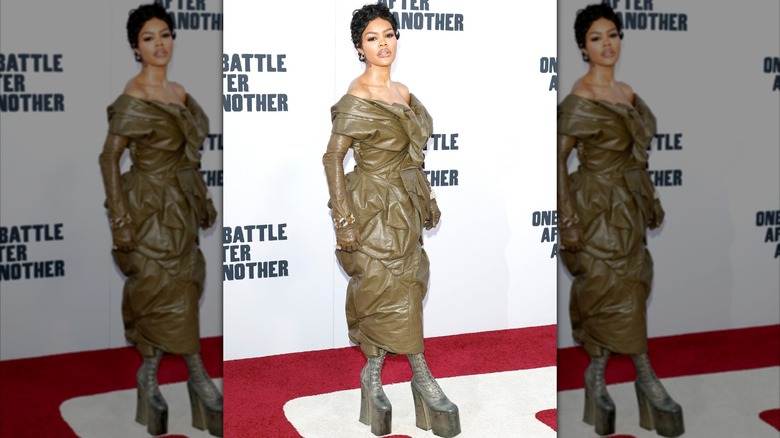 Teyana Taylor posando en una alfombra roja luciendo un vestido de cuero verde oliva con botas de plataforma.