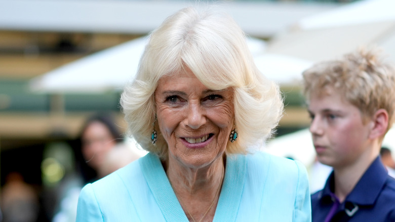 La reina Camilla viste un bob de plumas y una chaqueta de traje azul.