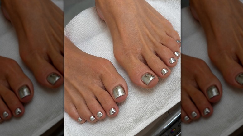Dos pies con pedicura cromada plata.