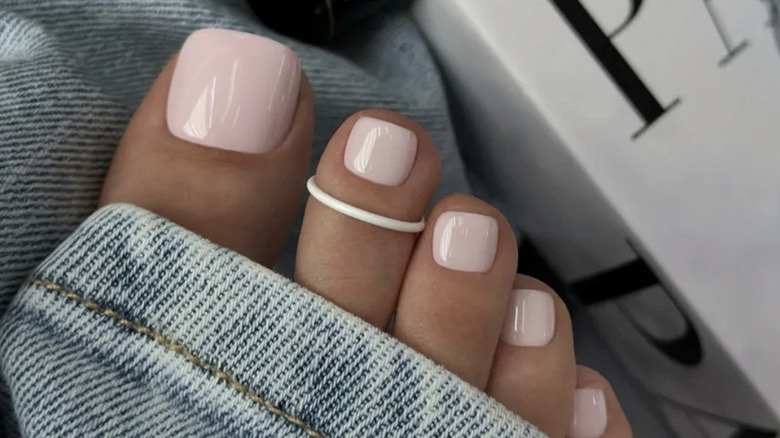 Pedicura rosa bebé con un anillo blanco en el segundo dedo