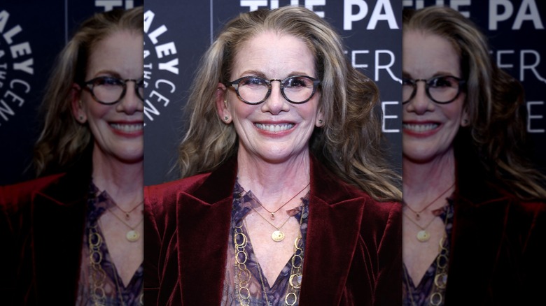 Melissa Gilbert sonríe con gafas redondas y un blazer de terciopelo rojo