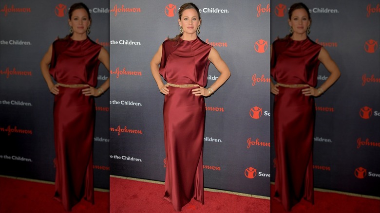 Jennifer Garner posando en una alfombra roja con un vestido de satén rojo rubí con un cinturón color canela.