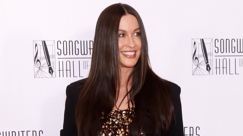 Alanis Morissette con cabello lacio luciendo un top dorado brillante y una chaqueta negra en la alfombra roja.