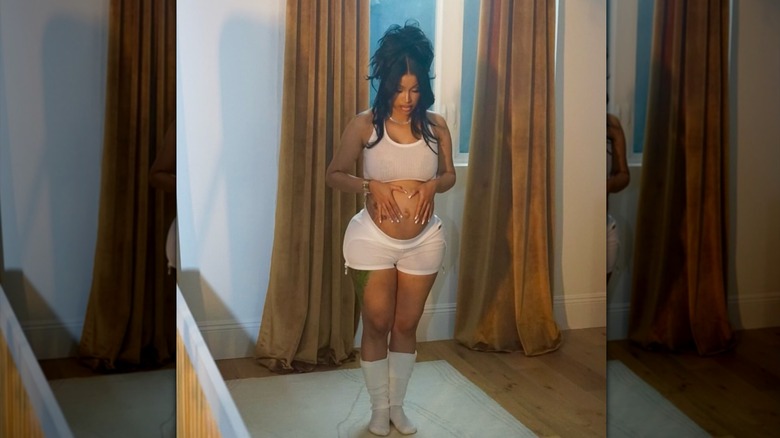Cardi B sosteniendo su panza mientras usa un traje de baño blanco