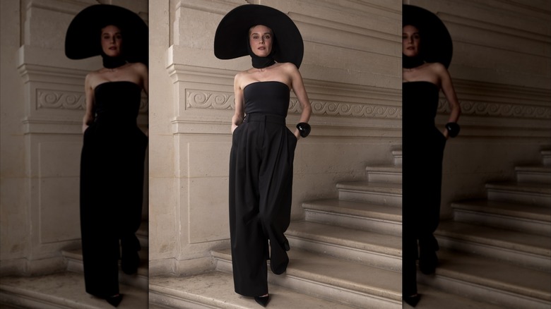 Diane Kruger vistiendo un mono negro sin tirantes con una gargantilla negra y un sombrero negro de ala ancha.