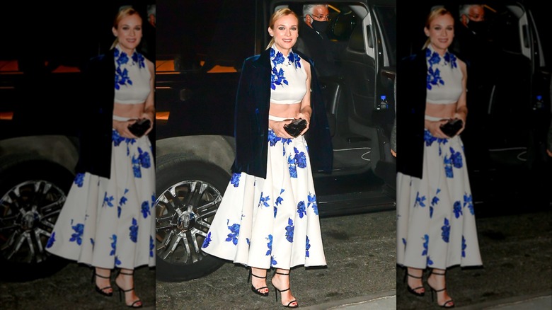 Diane Kruger en un evento luciendo un conjunto de falda y top corto floral de dos piezas en blanco y azul con una chaqueta de terciopelo azul oscuro.