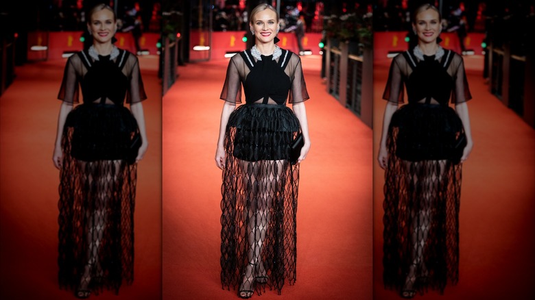 Diane Kruger en la alfombra roja con un vestido negro con mangas transparentes y pantalones cortos negros cubiertos con una falda larga de encaje negro.
