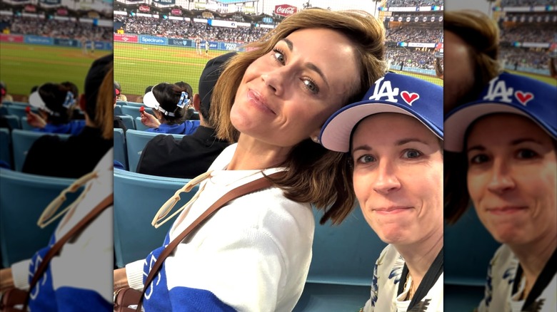 Nikki DeLoach posa para una selfie con su amiga Aimee Parker, ambas vestidas con ropa deportiva y asistiendo a un partido de béisbol.