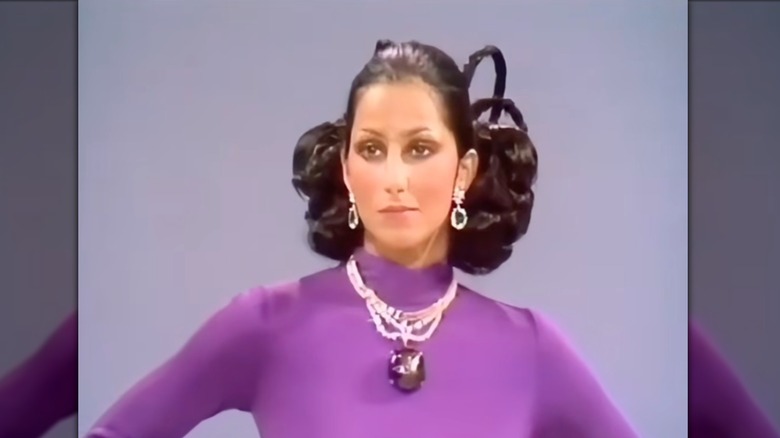 Cher con un vestido morado y un collar de cristal de zafiro.