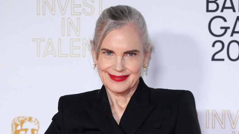 Elizabeth McGovern en un evento de alfombra roja con un top negro con lápiz labial rojo brillante y cabello gris recogido en un recogido.