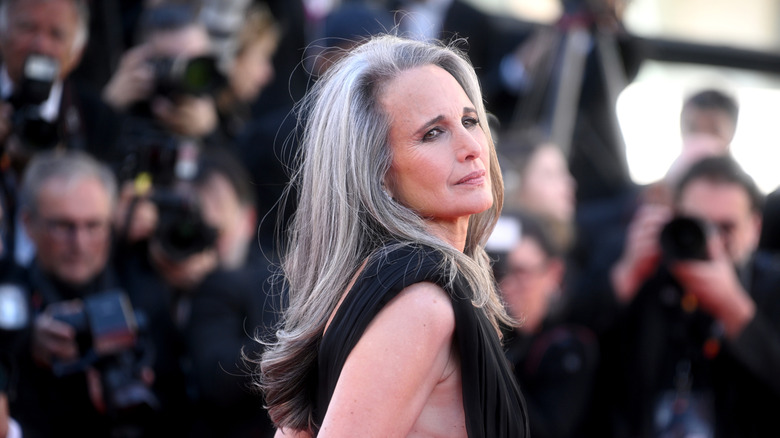 Andie MacDowell en la alfombra roja con un vestido negro y cabello largo y gris.