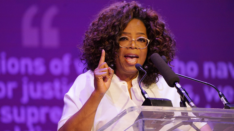 Oprah Winfrey habla por un micrófono en el escenario frente a un fondo morado.
