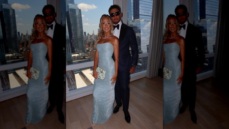 Brittany Mahomes y Patrick Mahomes posan juntos frente a una ventana con vista al horizonte de Nueva York.