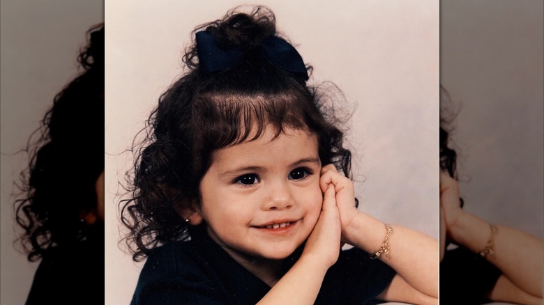 Una Selena Gomez de bebé posa con las manos en la mejilla.
