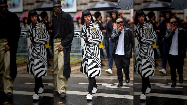 Una mujer durante la Semana de la Moda de París 2024 viste un impermeable a rayas blancas y negras con mocasines blancos.