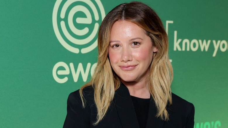 Ashley Tisdale con una chaqueta negra y sonriendo con el pelo suelto.