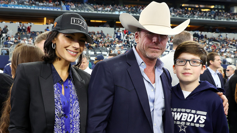 Nicole, Taylor y Gus Sheridan posan juntos en un evento deportivo con una multitud de fondo.