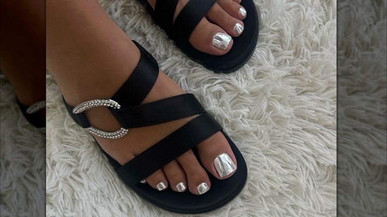 Primer plano de los pies de una mujer con una pedicura cromada plateada, con sandalias negras