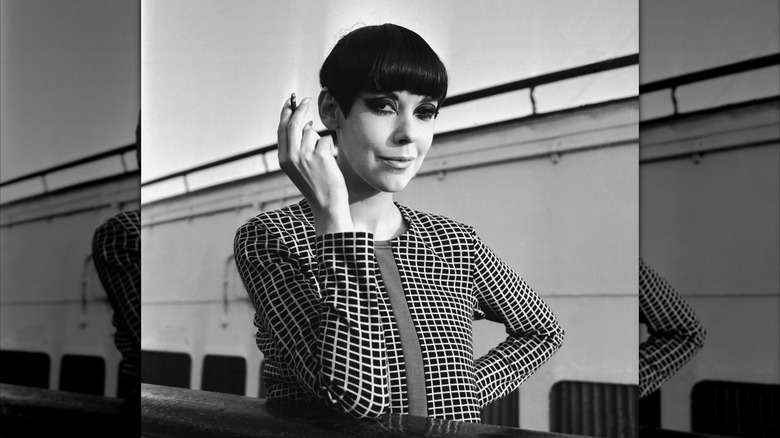 Un retrato de Peggy Moffitt sosteniendo un cigarrillo y sonriendo en blanco y negro