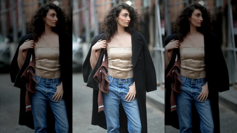 Una mujer viste una camisola de satén color canela, jeans azules y un abrigo de lana negro.