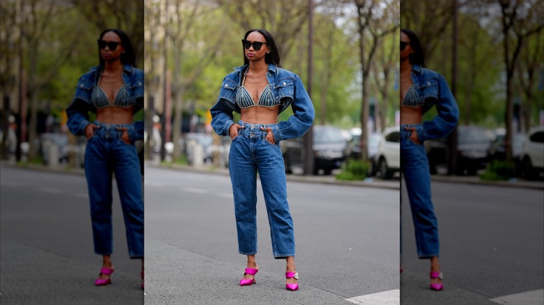 Una mujer viste jeans azules, un sujetador de mezclilla y una chaqueta de mezclilla corta.