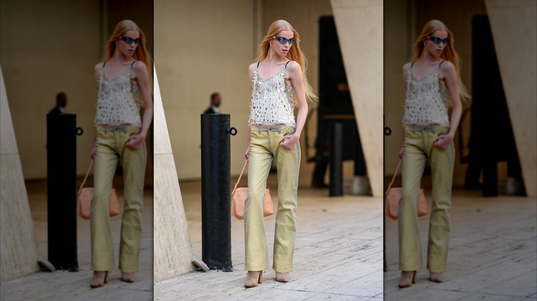 Una modelo en la Semana de la Moda de Nueva York de 2024 viste jeans de color amarillo claro y un top blanco cubierto de lentejuelas plateadas.