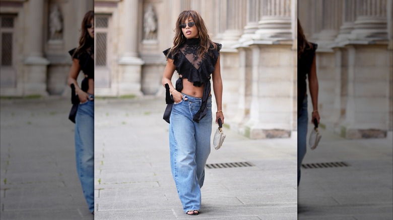 Una mujer vestida con jeans azules y un top corto con volantes y cuello alto.