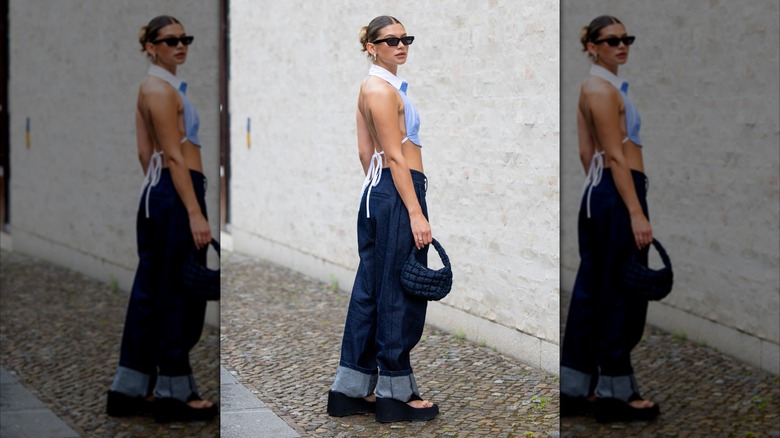 Una mujer en la Semana de la Moda de Berlín 2025 viste un top corto azul claro con la espalda expuesta y jeans holgados.