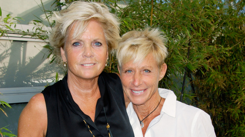 Meredith Baxter y su esposa Nancy Locke posan juntas frente al follaje verde del fondo.