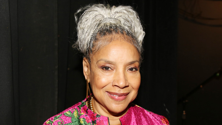 Phylicia Rashad sonríe luciendo su cabello gris recogido en un moño y una chaqueta rosa intenso.