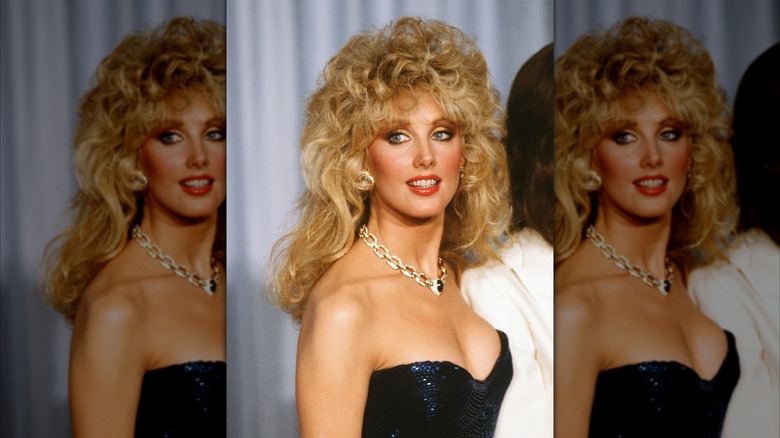 Morgan Fairchild posando con un vestido azul brillante y un collar de cadena de oro.