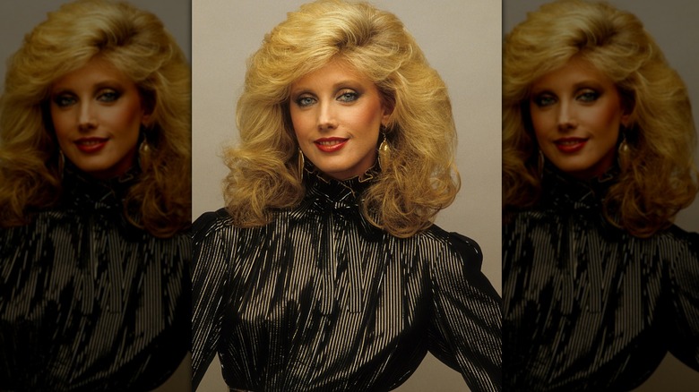 Morgan Fairchild posando con un top negro y aretes dorados.
