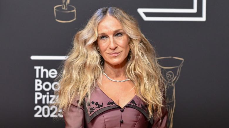 Sarah Jessica Parker posando en un evento luciendo un vestido granate con el pelo ondulado y un delicado collar.