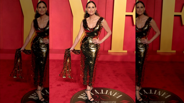 Minnie Driver posando en una fiesta de los Oscar con un vestido dorado reluciente.