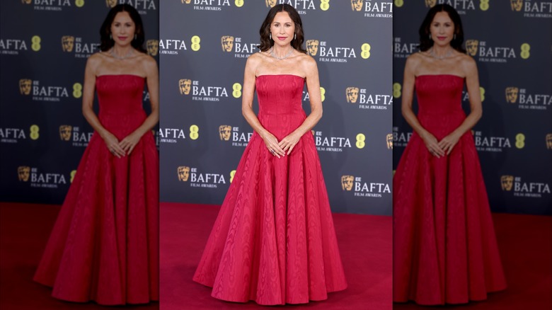 Minnie Driver posando en la alfombra roja con un vestido rojo sin tirantes.