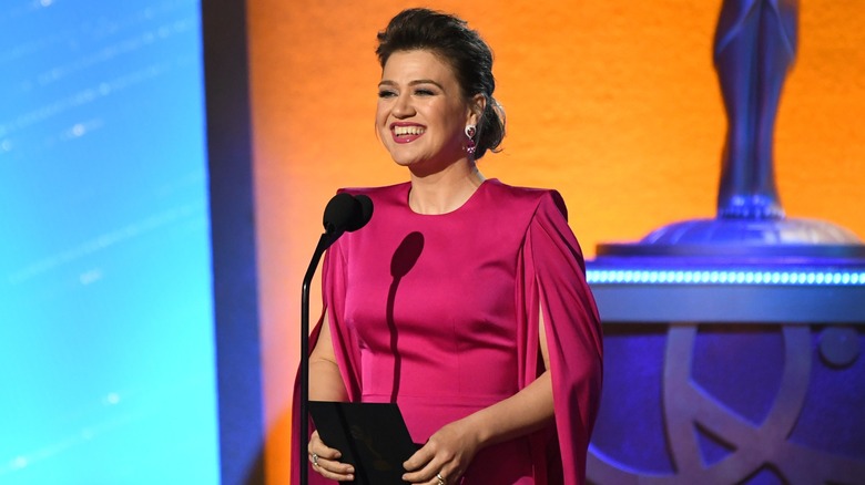 Kelly Clarkson presentando un premio en los Emmy 2024 con un vestido rosa oscuro.